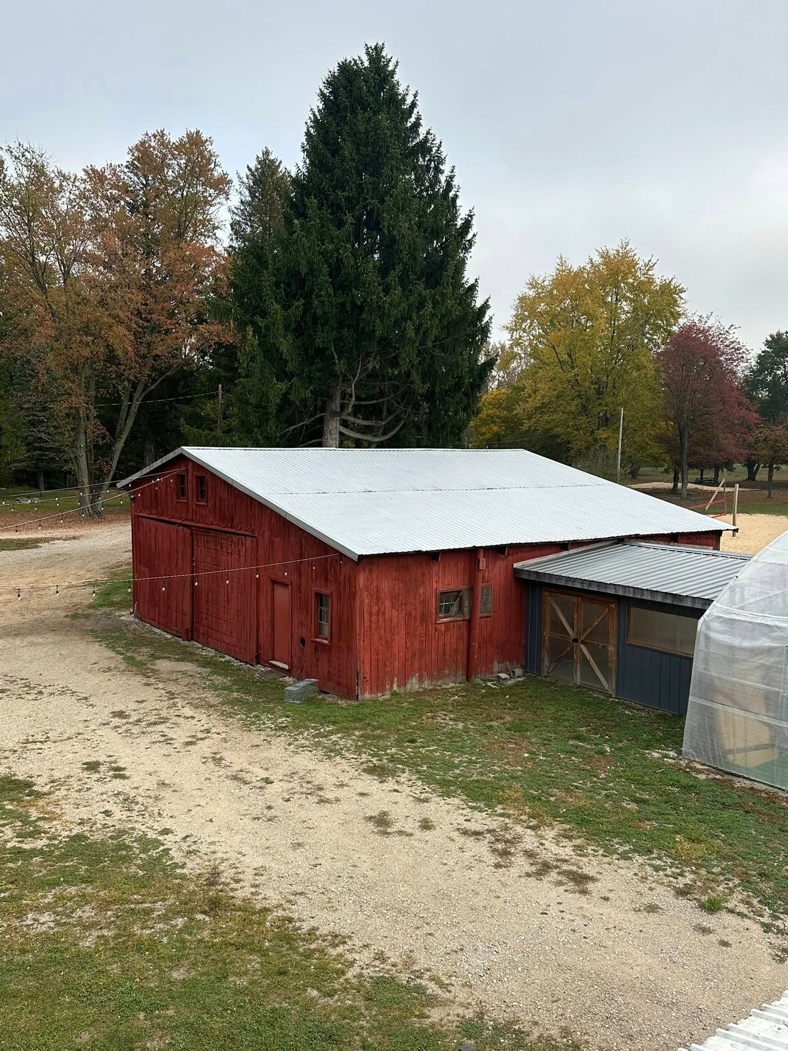 Red wooden barn with white roof beside a gravel path, surrounded by autumn trees.