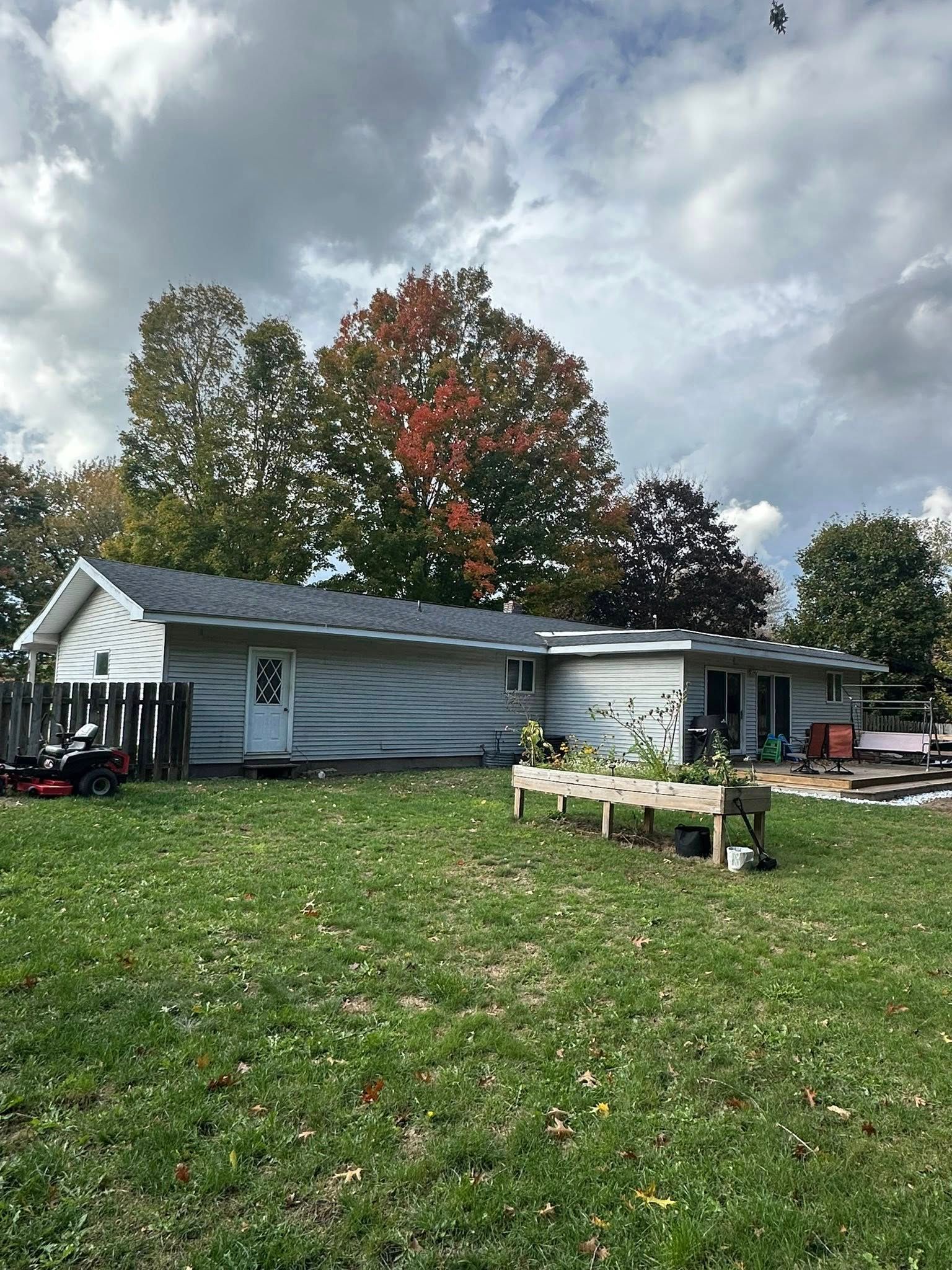White house with dark roof on a grassy lawn under cloudy sky, autumn trees behind it