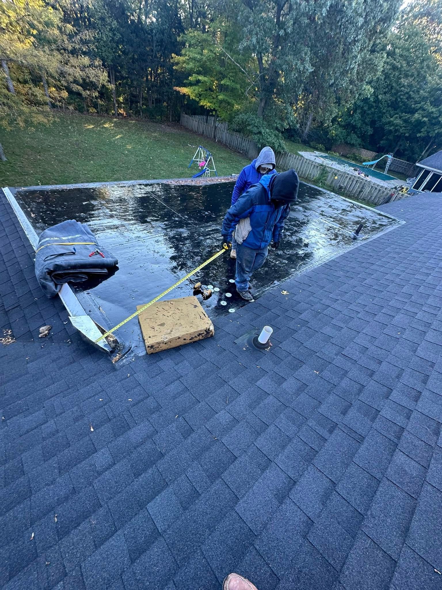 Worker in blue rain gear cleaning a roof near a skylight and gutter.