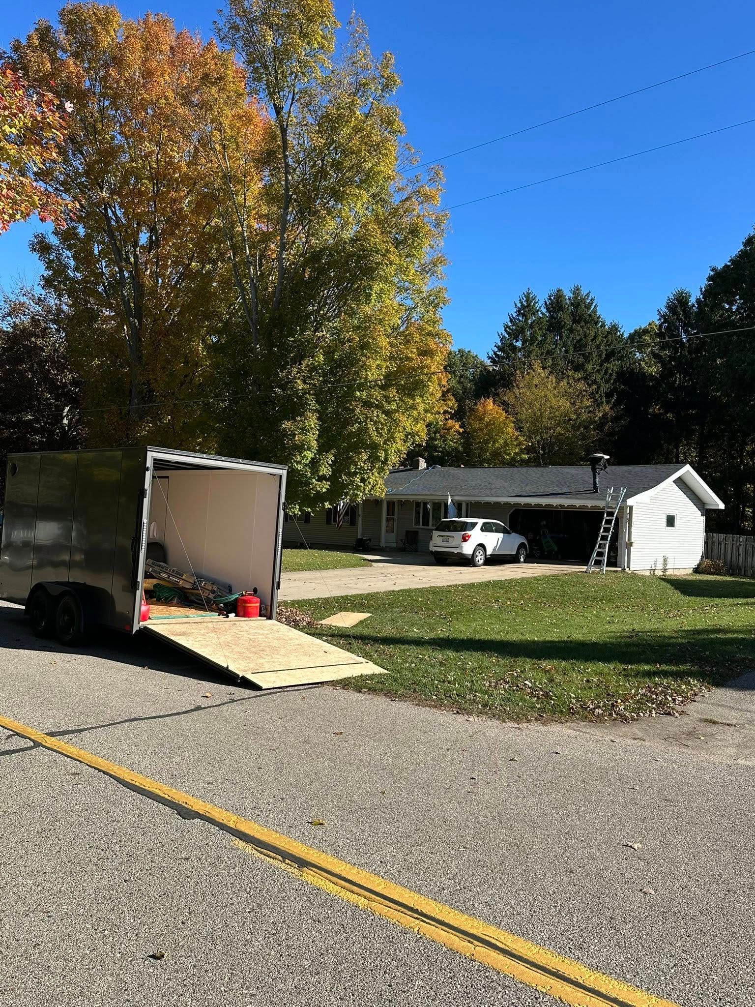 Outdoor scene with an open white trailer, gravel road, autumn trees, and a small house in the background