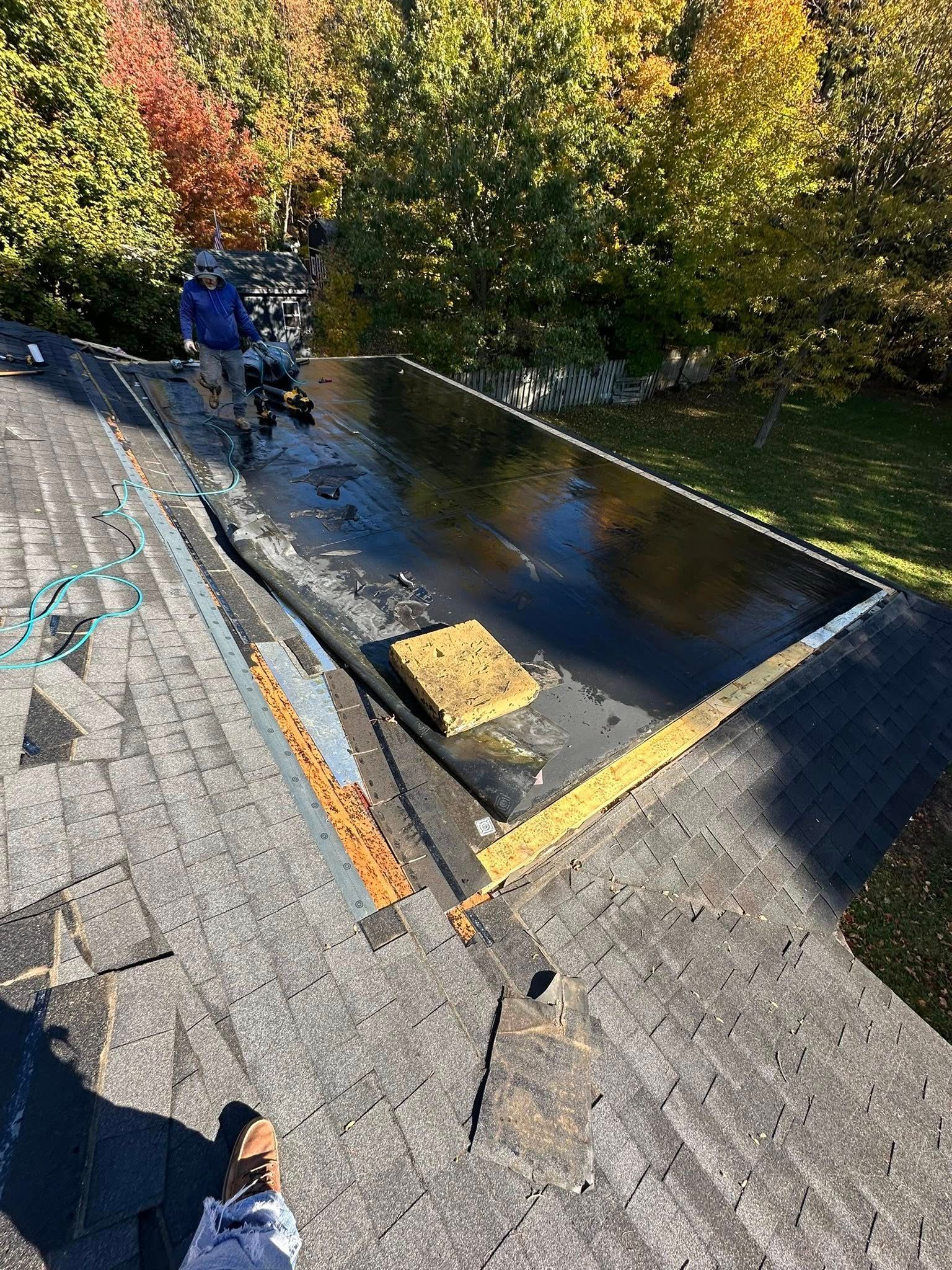 Worker cleaning debris from a flat rooftop with wet patches and autumn trees in the background