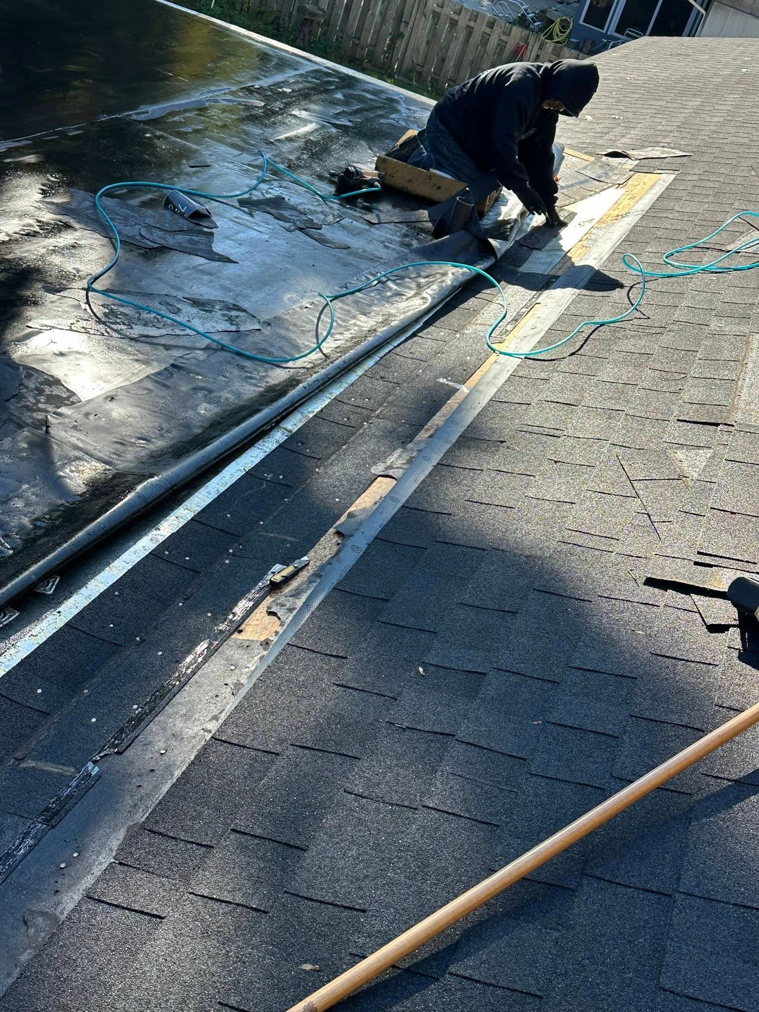 Worker kneeling on a wet roadside, cleaning or repairing a curb with tools and hoses.