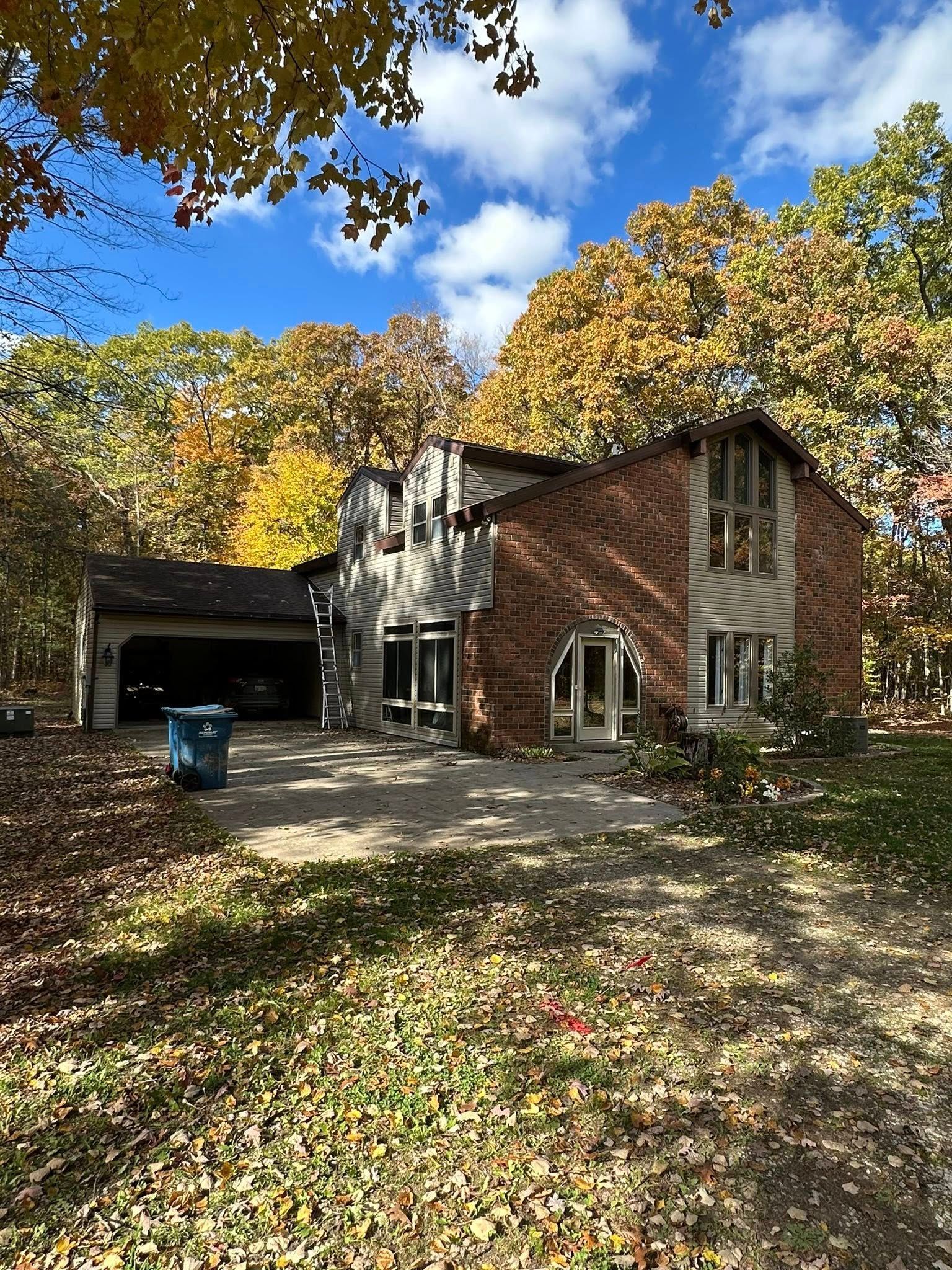 Suburban brick house with garage, blue bin, and autumn trees under a sunny sky