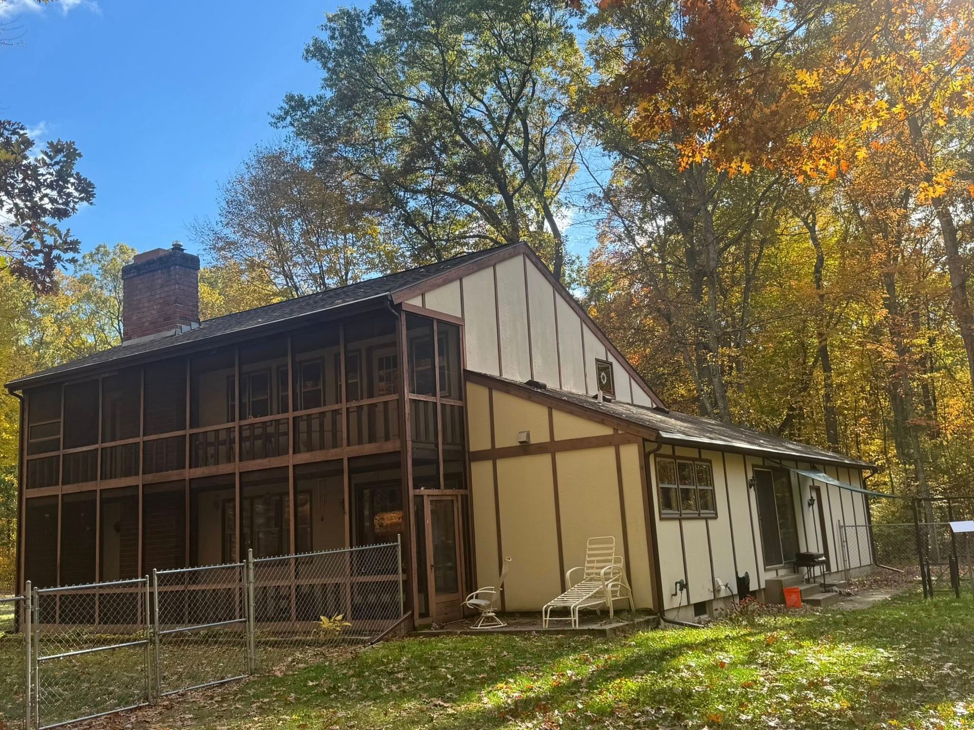 Old farmhouse with screened porch and white siding, surrounded by autumn trees under a blue sky