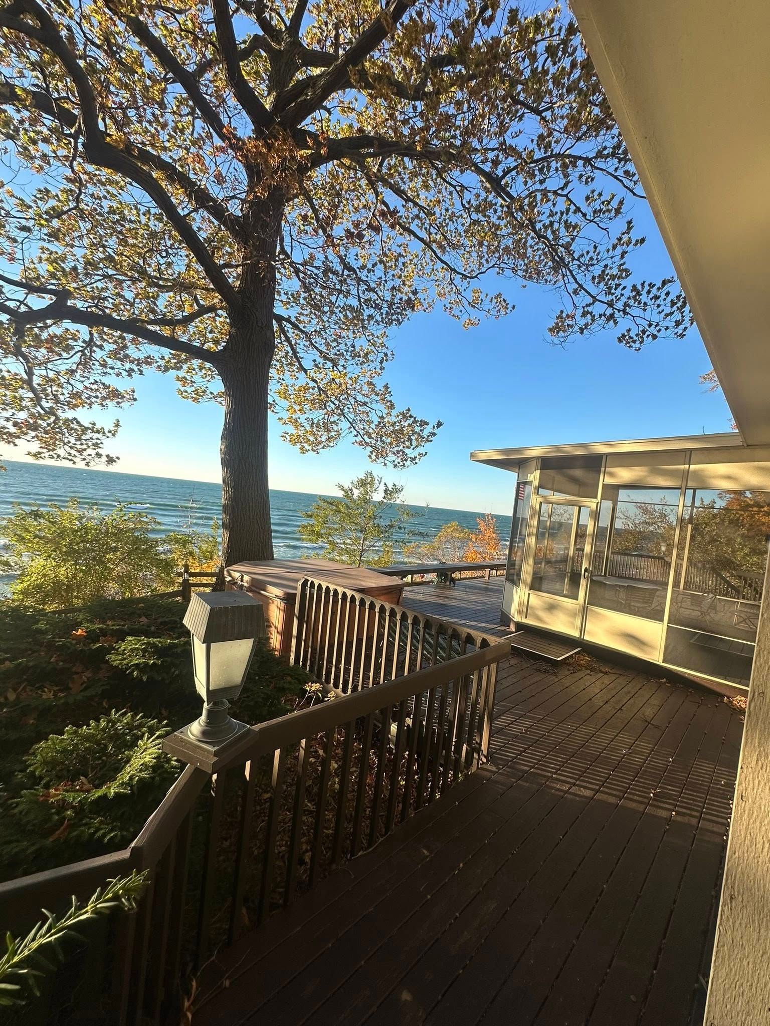 Wooden deck overlooking a lake and distant hills, framed by a large tree in warm sunlight