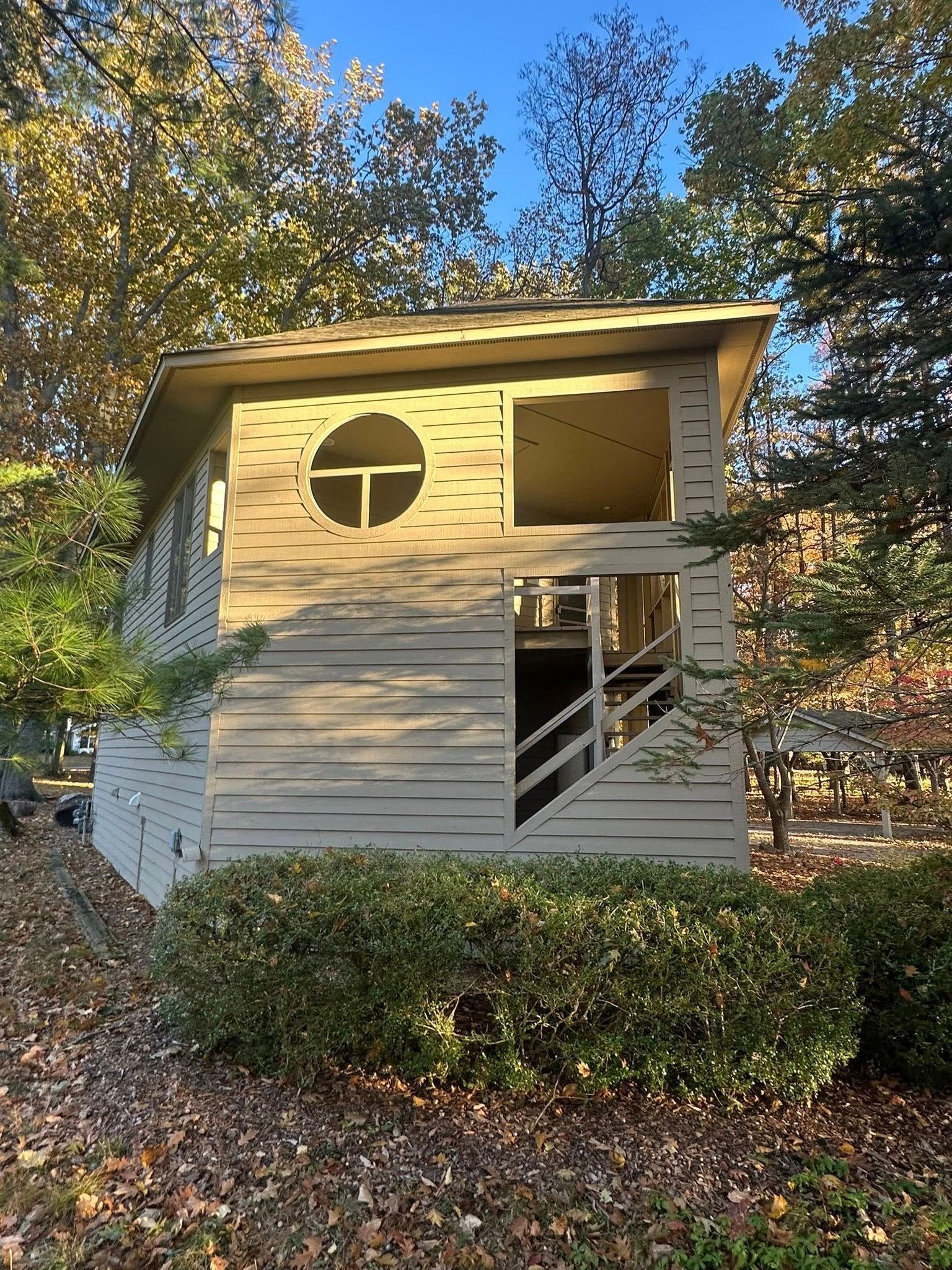 Small white treehouse with round and square windows among autumn trees and bushes.