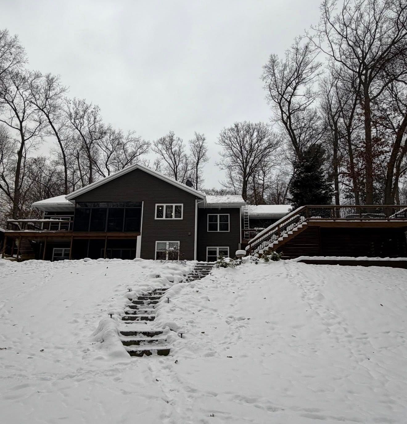 Snowy house with bare trees and stairs leading up a steep front yard