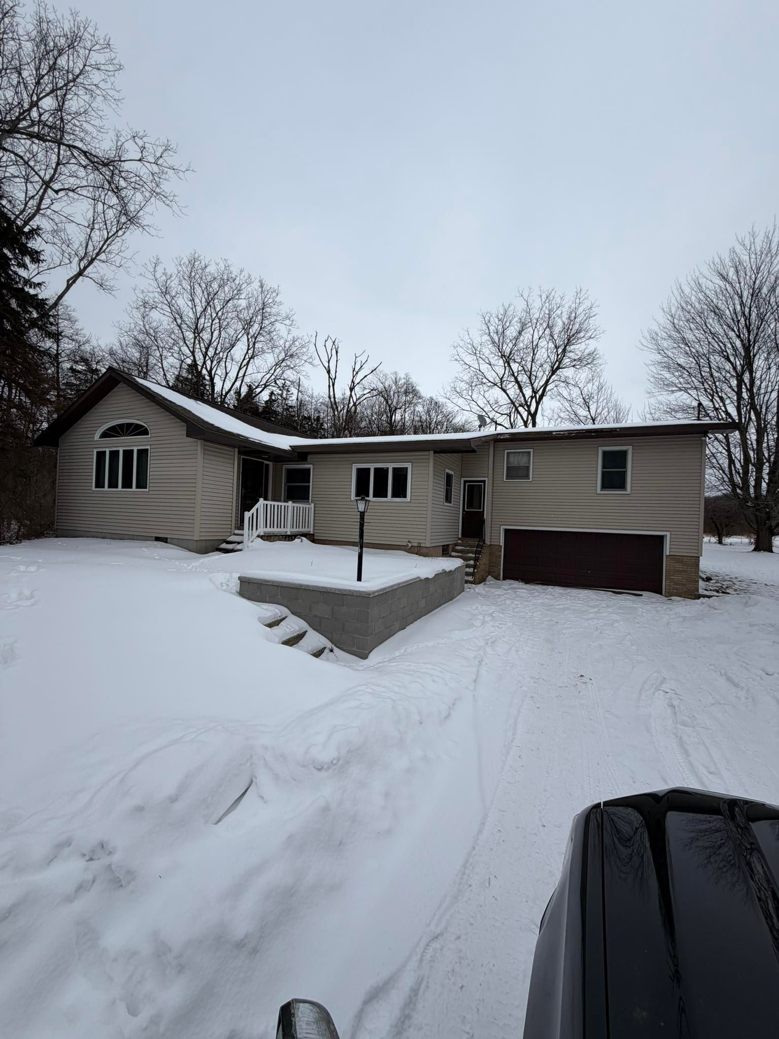 Snow-covered suburban house with driveway, front porch, and bare trees in winter.