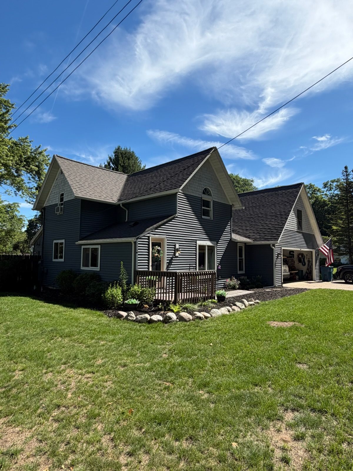 Gray house with black roof, stone chimney, and small front porch on a sunny grassy lot