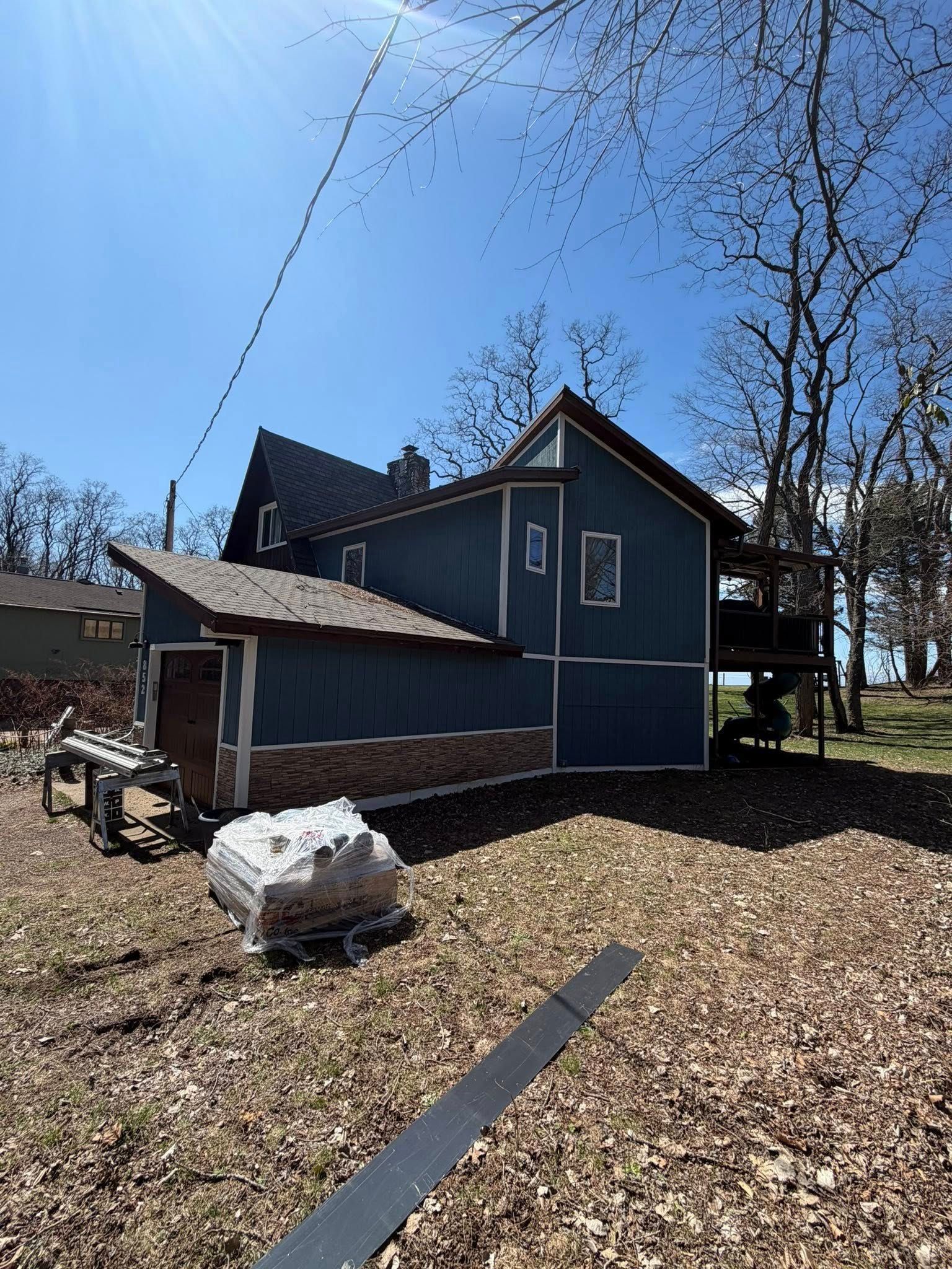 Blue house with steep roof and porch in a leaf-covered yard under a clear sky