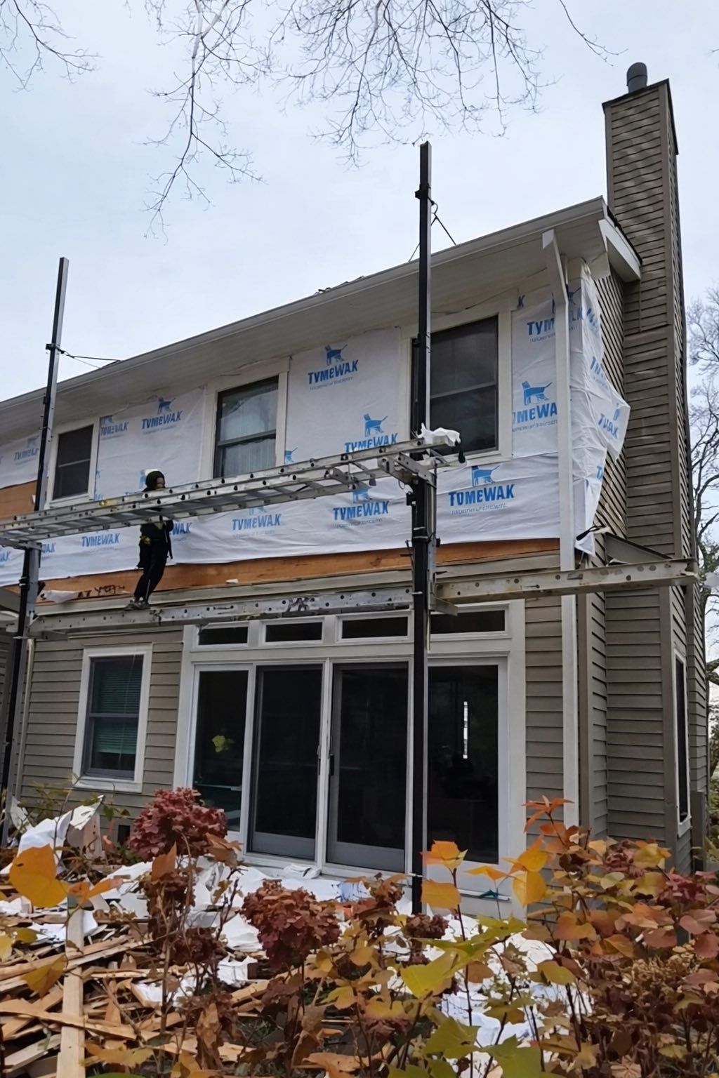 Partially renovated two-story house with wrapping and scaffolding in a snowy yard