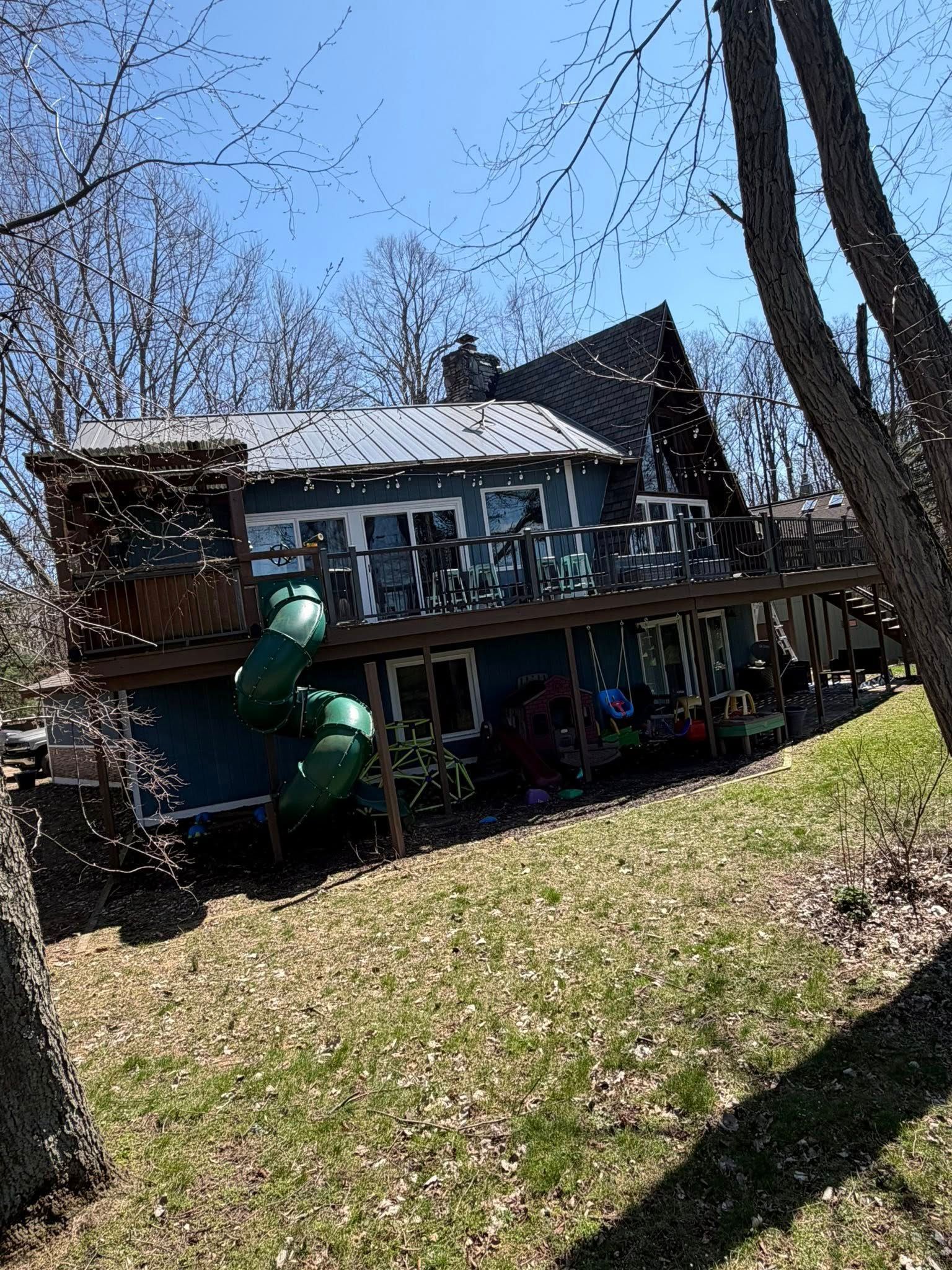 Backyard house with deck, leaf-covered lawn, and green dinosaur lawn ornament under a clear blue sky