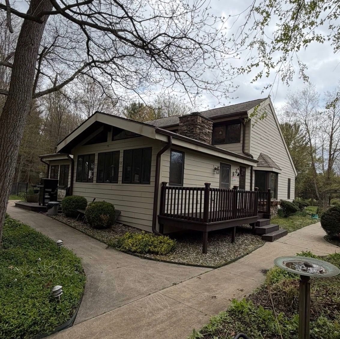 Suburban house with beige siding, front porch, and curved walkway surrounded by trees