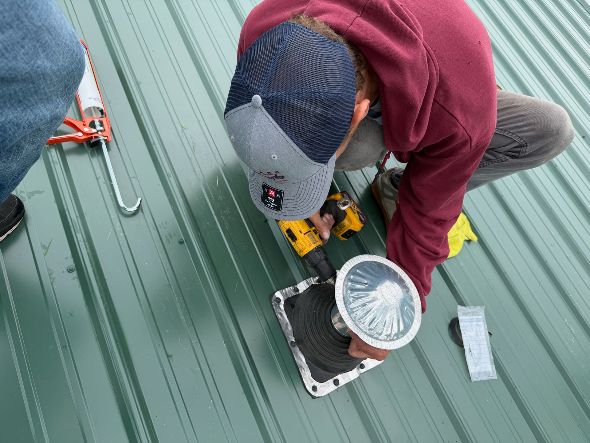 Worker using a drill to install a vent on a green metal roof