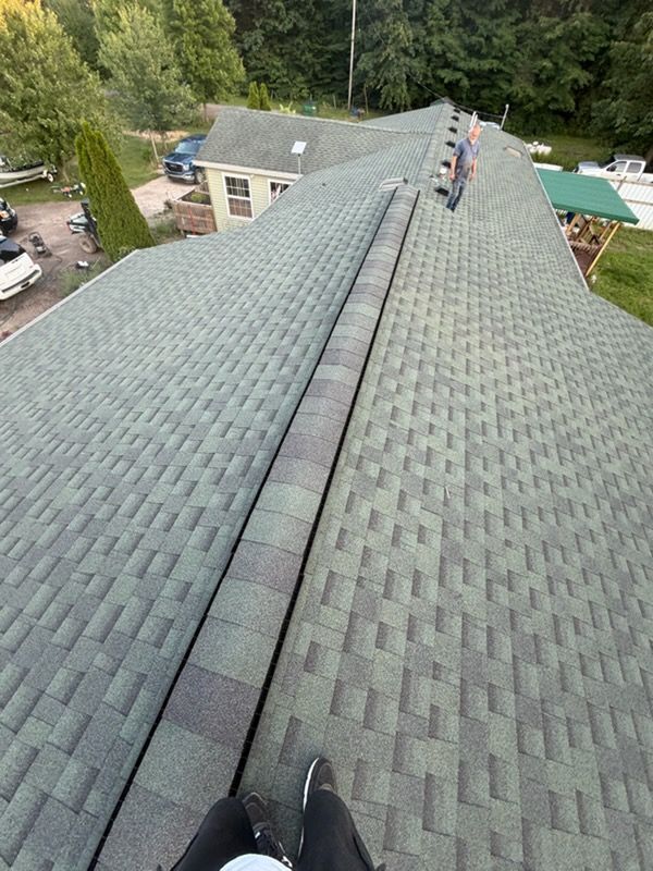 Roof with green shingles and a ridge vent, viewed from above on a house surrounded by trees.
