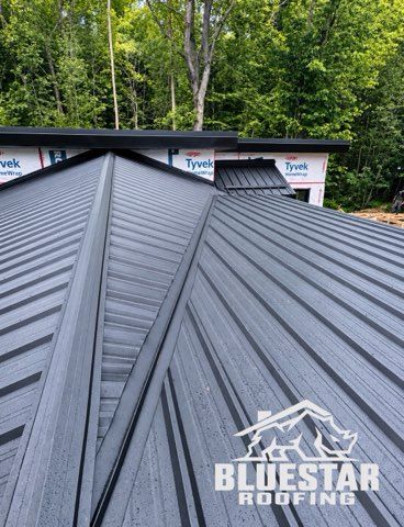 Dark gray metal roof with standing seams on a house under construction, surrounded by trees