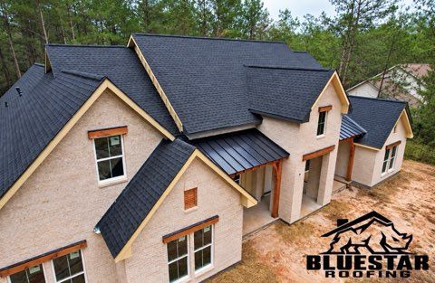 Aerial view of a new beige house with dark gray roofing and a Bluestar Roofing watermark