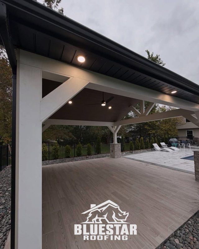 Covered outdoor deck at dusk with wood flooring, white beams, and lounge chairs by a pool.