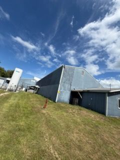 Industrial buildings beside a grassy slope under a bright blue sky with clouds