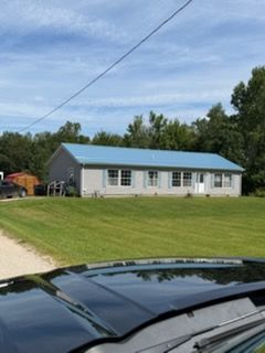 Single-story white building with a blue roof on a grassy lot, seen from a car windshield.