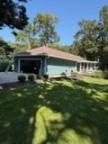 Single-story teal house with a covered porch, driveway, and sunlit lawn under blue sky