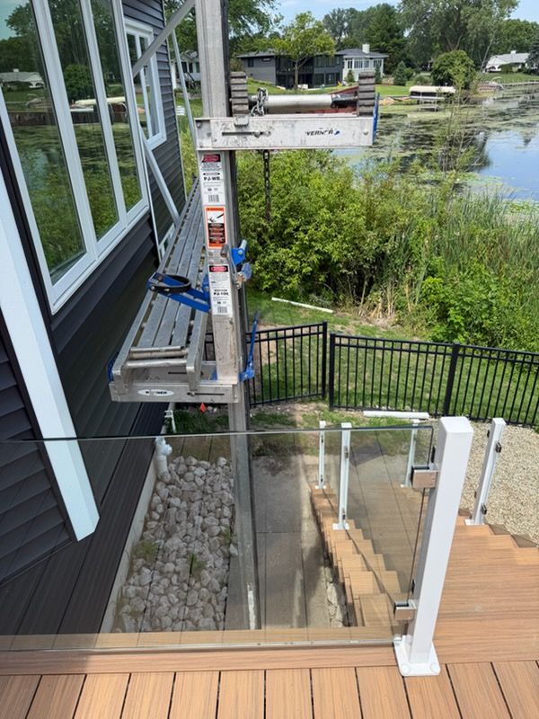 Construction lift outside a house beside a glass-railed balcony, overlooking water and trees