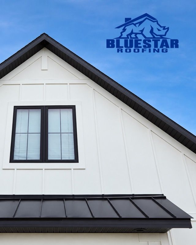 White house gable with black-trimmed windows and roof, BlueStar Roofing logo in the blue sky above.