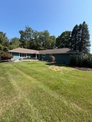 Single-story teal house with a large green lawn and trees under a clear blue sky
