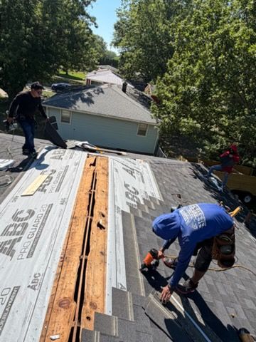 Workers installing roofing on a house, with underlayment exposed and trees in the background