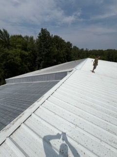 White metal roof with a worker near the ridge and trees in the background