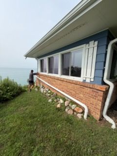 Person standing by a lakeside house with white-trimmed windows and brick siding