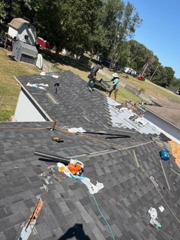 Roof under repair with scattered shingles and tools on a house in a tree-lined neighborhood