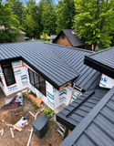 Roofing crew installing dark gray metal roofing on a house surrounded by green trees