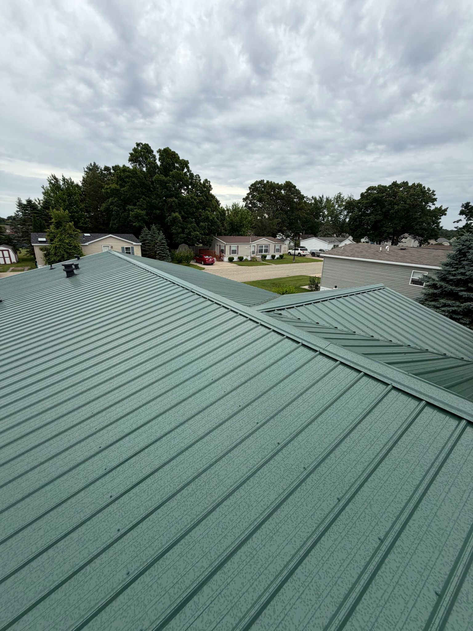 Green metal roof with trees and cloudy sky in the background