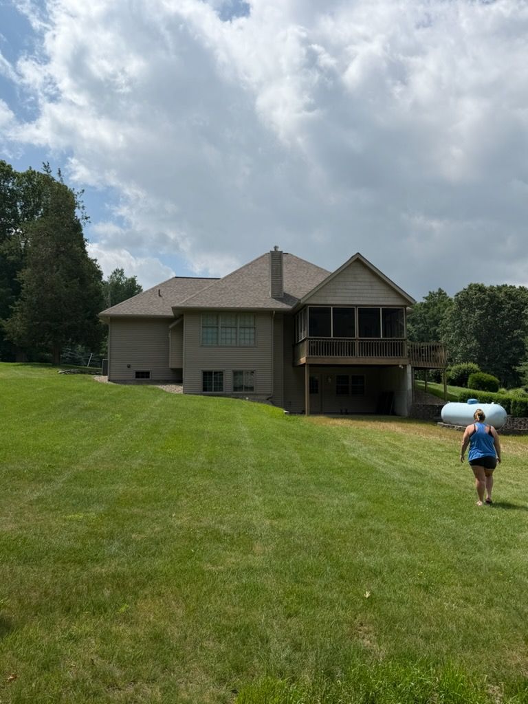 Person carrying a white float walks across a grassy yard toward a house under cloudy skies