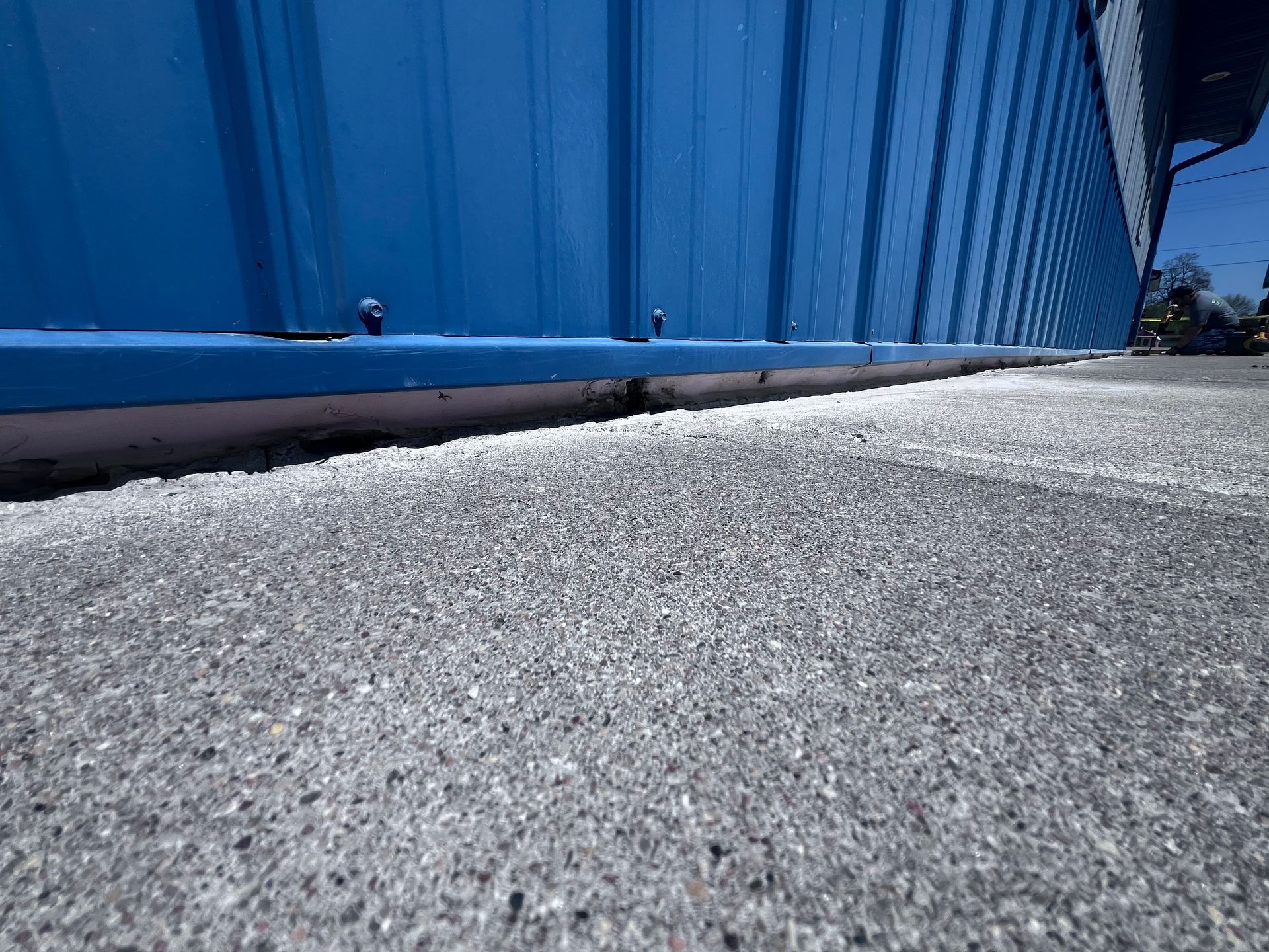 Blue corrugated metal wall beside a sunlit rough concrete surface outdoors