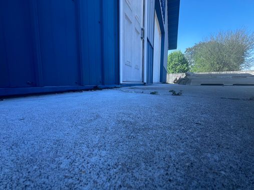 Low-angle view of a blue building entrance beside a concrete walkway and trees under a clear sky