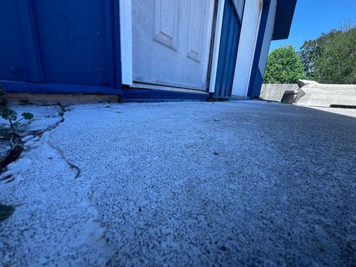 Close-up of cracked concrete walkway beside a blue building and white door in bright sunlight