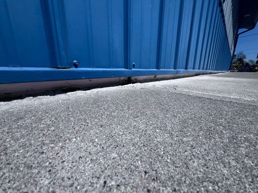 Blue metal wall beside a rough gray pavement under bright sunlight