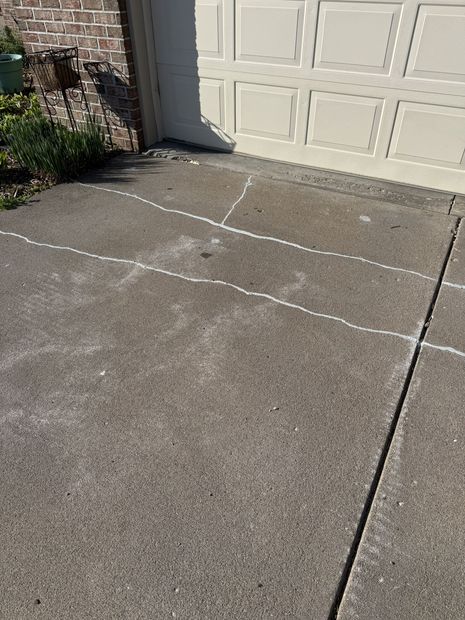 Cracked concrete driveway next to a white garage door with chalk lines marking the surface
