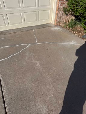 Cracked driveway apron in front of a garage door, with white repair lines on the pavement.