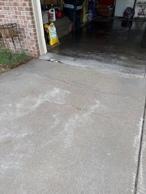 Concrete driveway leading into an open garage with cleaning supplies visible inside.