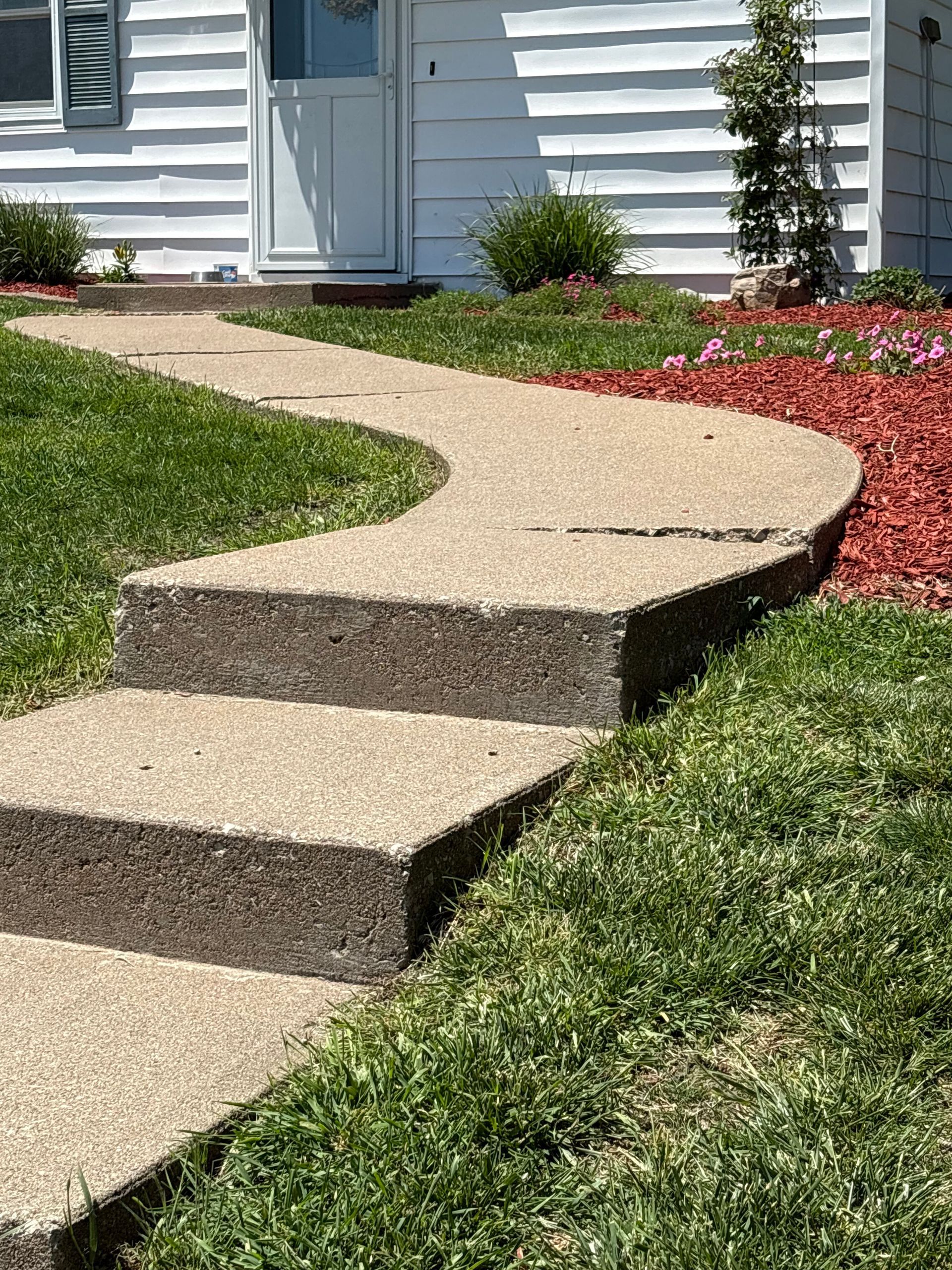 Curved front walkway with low steps leading to a house entrance and flower bed.