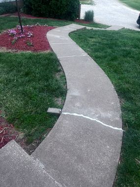 Curved concrete sidewalk winding through a grassy yard beside a red flower bed and street