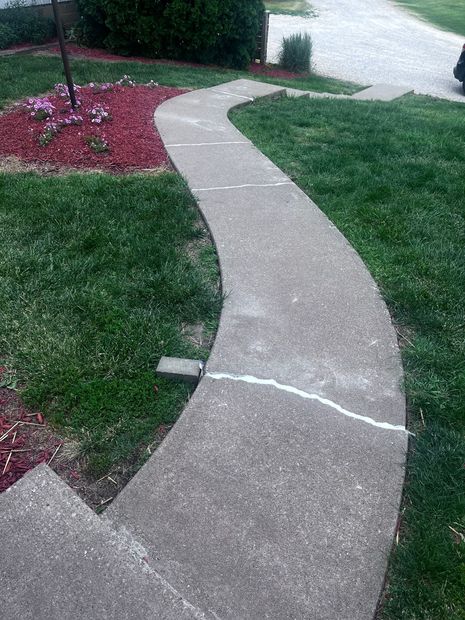 Curved concrete sidewalk winding through a grassy yard beside a red flower bed and street