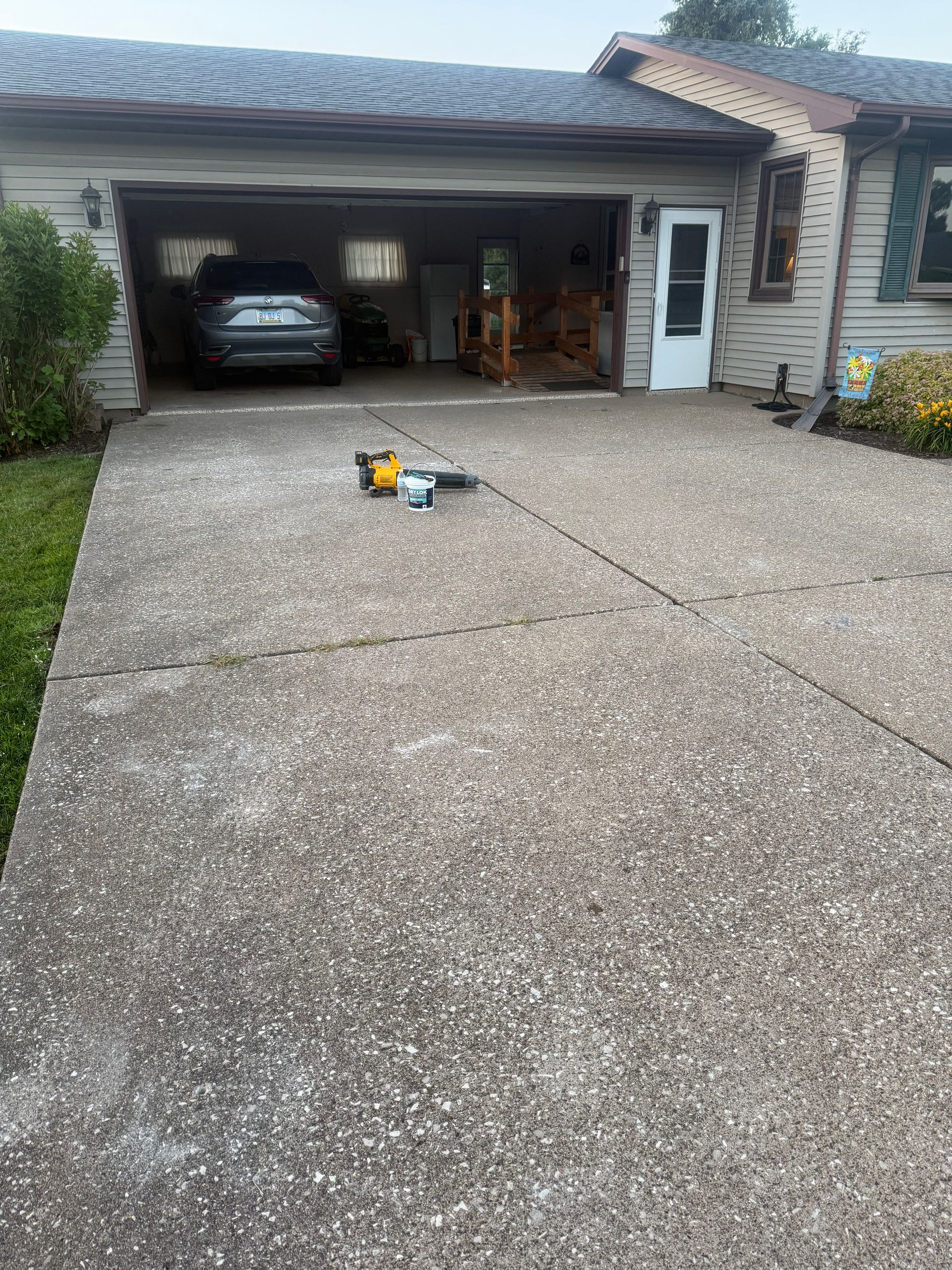 Driveway view of an open garage with a parked car, tools on the concrete, and a side entrance door.