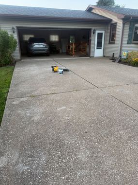 Driveway leading to an open garage with parked car and tools on the ground