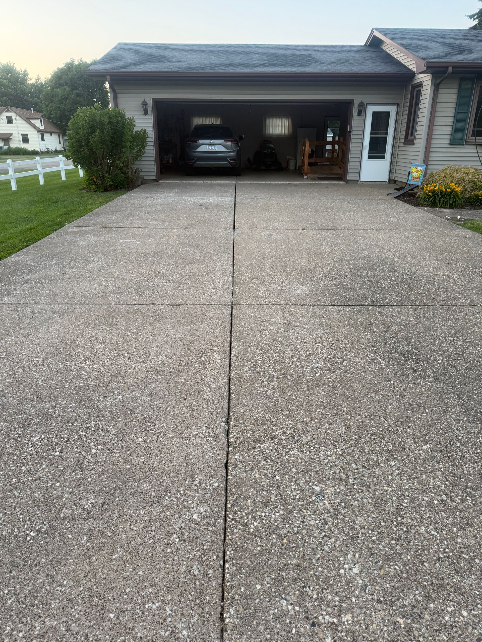 Driveway leading to an open garage with a car inside, beside a house at dusk.