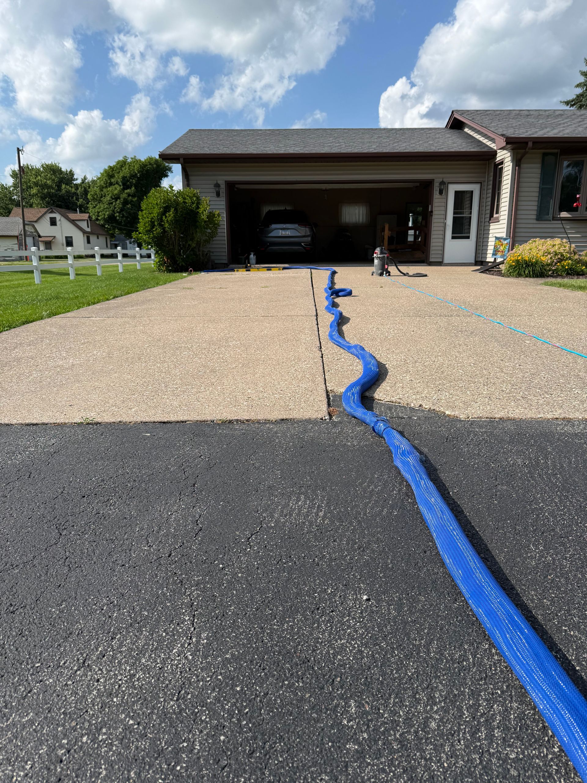 Driveway with a blue hose or cable running to a garage under a partly cloudy sky.