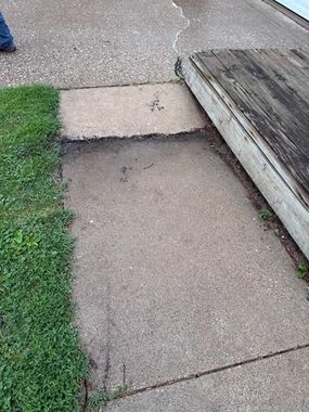 Uneven concrete sidewalk beside grass and a wooden ramp edge
